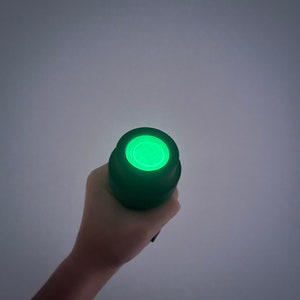 May include: A black flashlight with a green light shining from the end.