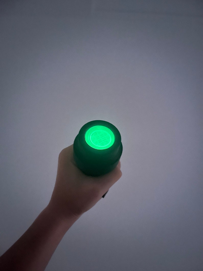 May include: A black flashlight with a green light shining from the end.