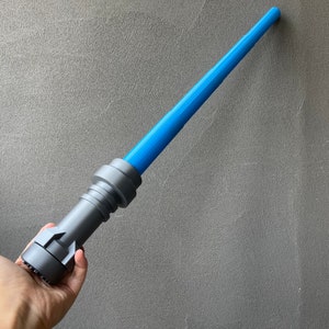 May include: A blue and gray lightsaber toy. The lightsaber is made of plastic and has a blue blade. The lightsaber is held in a person's hand.
