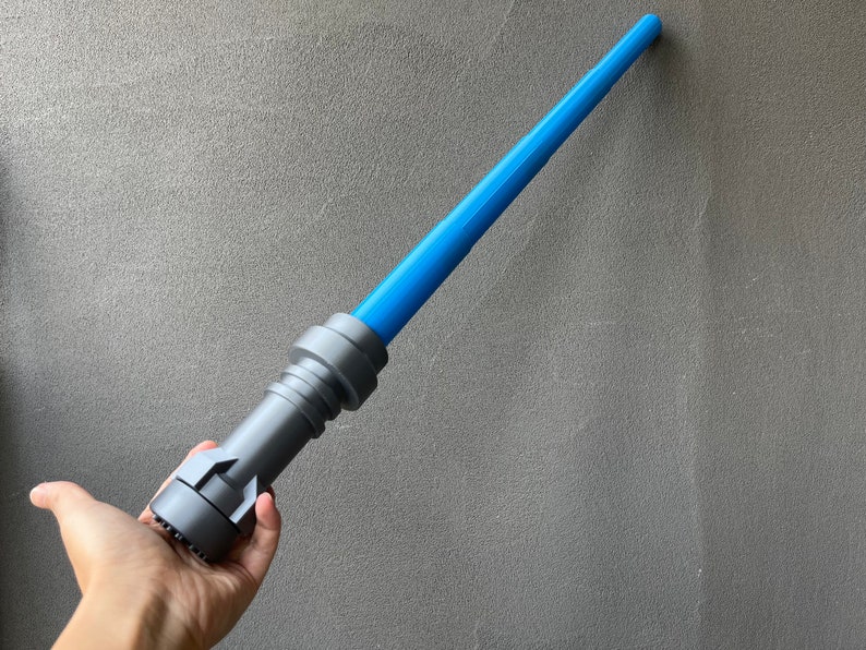 May include: A blue and gray lightsaber toy. The lightsaber is made of plastic and has a blue blade. The lightsaber is held in a person's hand.