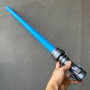 May include: A blue and gray lightsaber toy with a handle that has a textured surface.