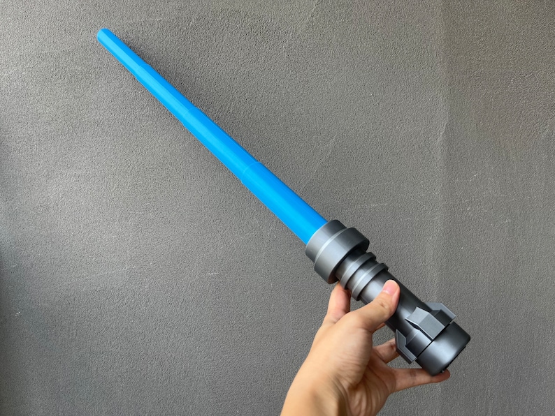 May include: A blue and gray lightsaber toy with a handle that has a textured surface.