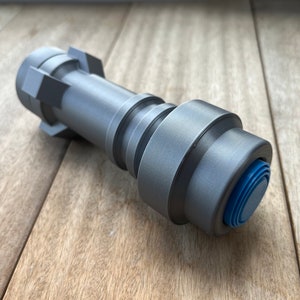May include: A silver-colored metal lightsaber hilt with a blue button on the end.