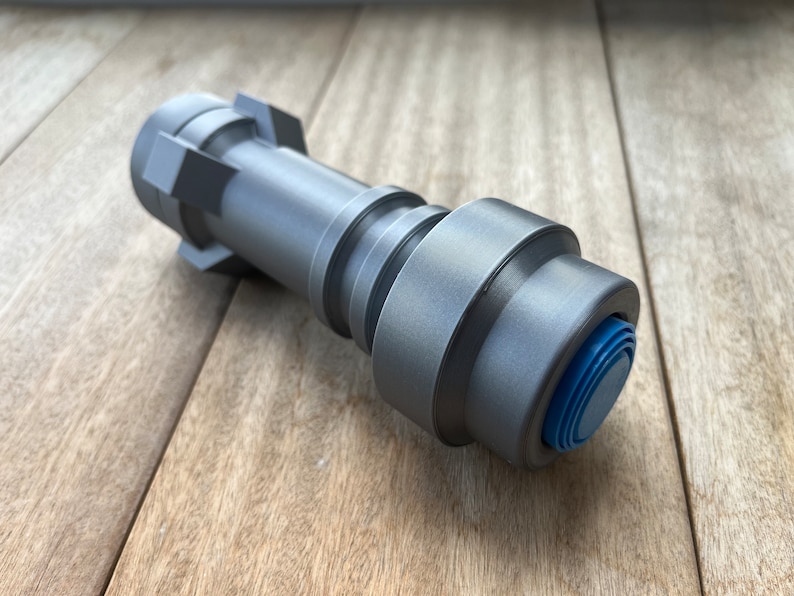 May include: A silver-colored metal lightsaber hilt with a blue button on the end.