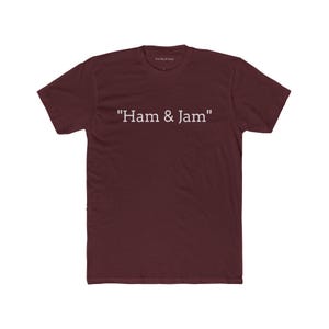 Op de afbeelding: Bordeauxrood t-shirt met de witte tekst "Ham & Jam" in het midden op de voorkant. Het shirt heeft korte mouwen en een ronde hals. De merknaam "The Much Gear" staat bovenaan.