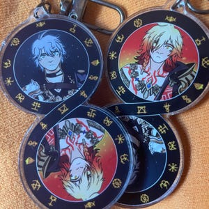 May include: A collection of circular keychains featuring anime-style character illustrations. Each keychain has a black border with gold symbols and a silver keyring. The character art includes a person with blue hair, and a person with red and yellow hair.
