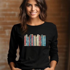 May include: A black long-sleeve shirt with a graphic of a row of vintage books. The books have colorful spines and titles like "The Little Prince" and "Pride and Prejudice".