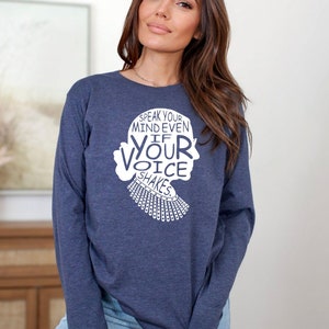 May include: A navy blue long-sleeved shirt with a white graphic of a woman's silhouette and the text "Speak your mind even if your voice shakes".