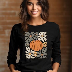May include: Black long-sleeve shirt with a vintage-style graphic of a pumpkin surrounded by flowers. The flowers are in shades of gray, white, and yellow.