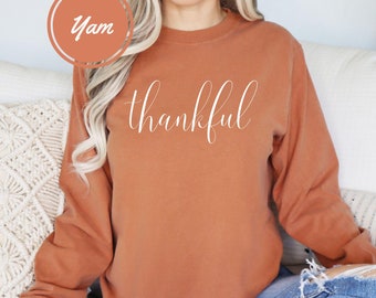 May include: A rust-colored long-sleeved sweatshirt with the word "thankful" written in white cursive lettering.