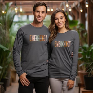 May include: Two people wearing long-sleeved shirts with the text "EMERGENCY" printed in colorful letters. The shirts are a dark charcoal grey color.