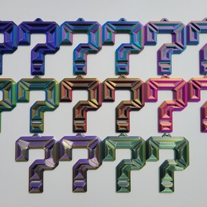 May include: A set of 12 iridescent question mark charms in various colours, including blue, green, purple, and gold. The charms are made of metal and have a 3D design.
