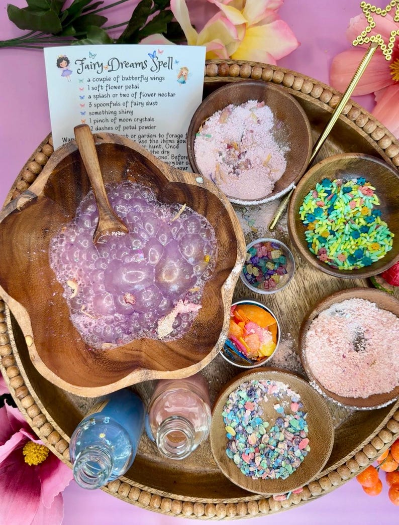 May include: A wooden tray with various bowls containing colorful ingredients for a fairy dream spell. The ingredients include flower petals, fairy dust, moon crystals, and petal powder. A list of ingredients is written on a card in the upper left corner of the image. The card reads "Fairy Dreams Spell".