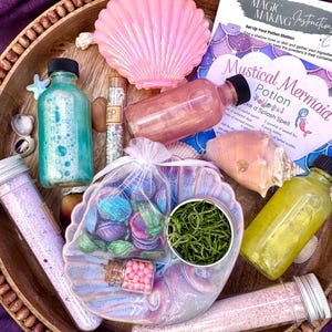 Peut inclure: Un kit de fabrication de potions comprenant un récipient en forme de coquillage rose, des flacons en verre remplis de liquides bleu, rose et jaune, un sachet en organza blanc avec des coquillages irisés, des perles roses, de la mousse verte et une carte.