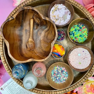 May include: A wooden tray with various bowls filled with colorful sprinkles, glitter, and other decorative items. There are also three small bottles with colorful liquids.