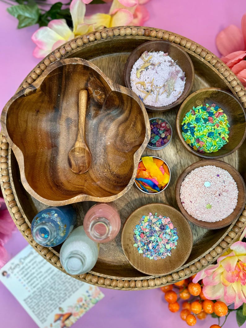 May include: A wooden tray with various bowls filled with colorful sprinkles, glitter, and other decorative items. There are also three small bottles with colorful liquids.