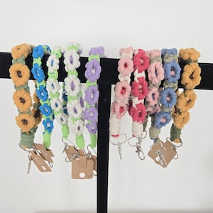 May include: Assortment of colorful crocheted flower-shaped keychains with metal rings. The keychains are displayed on a black stand.