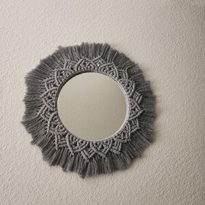 May include: A gray macrame mirror with a circular mirror and a fringe border.