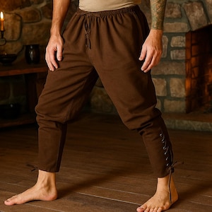 May include: Brown medieval-style pants with a drawstring waist and lace-up details on the lower legs. The pants are made of a soft fabric and are suitable for historical reenactments or themed events.