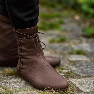 May include: Brown leather ankle boots with a lace-up design. The boots have a rounded toe and a flat sole. The boots are made of a soft, supple leather and appear to be comfortable for walking.