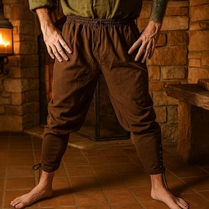 May include: Brown medieval-style pants with a drawstring waist and buttoned cuffs. The pants are made of a soft fabric and are designed to be comfortable. The pants are suitable for historical reenactments or costume events.
