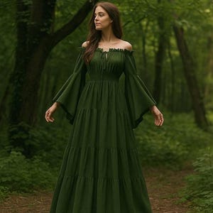 May include: A floor-length, dark olive green dress featuring an off-the-shoulder neckline with a ruffled trim, long flared bell sleeves, and a cinched waist. The skirt is constructed with multiple horizontal tiers, creating a full, flowing silhouette.