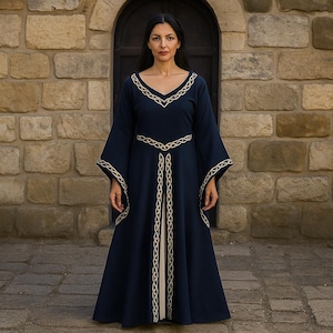May include: A navy blue dress with long, flared sleeves and a V-neck. The dress is adorned with gold-coloured trim around the neckline, sleeves, and front. The woman is standing in front of a stone wall.
