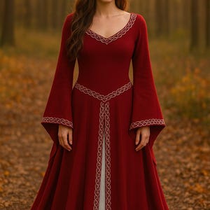 May include: A full-length, crimson dress with long, flared sleeves and a V-shaped neckline. The dress is adorned with gold-coloured embroidery around the neckline, sleeves, and waist. The dress is worn in a forest.