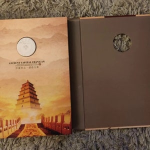 以下が含まれることがあります： 茶色の表紙の閉じた本で、夕焼けを背景にパゴダが写っています。本のタイトルは「古代の都長安」です。