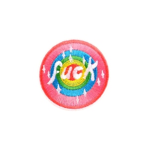 May include: Circular embroidered patch with a rainbow design and the word "fuck" in white script. The patch has a pink outer ring, with concentric rings of blue, green, yellow, and pink. Small white starbursts are scattered around the design.