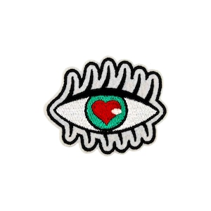 May include: A white eye with a green iris and a red heart in the center. The eye is surrounded by a black outline and white eyelashes.