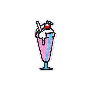 May include: Embroidered patch of a pink milkshake in a tall glass. The milkshake is topped with white whipped cream, a red cherry, and a blue straw. The patch is outlined in black with a white background.