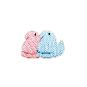 May include: Embroidered patch featuring two stylized bird-like figures. One is pink with a red belly band, the other is blue with a blue belly band. Both have black eyes and white outlines. The patch is designed to be ironed on or sewn onto fabric.