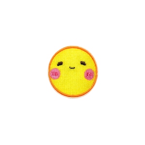 May include: A yellow embroidered patch with a smiling face and pink cheeks. The face has small black eyes and a small black mouth.