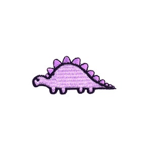 Könnte beinhalten: Lilafarbener gestickter Dinosaurier-Patch mit strukturiertem Design.
