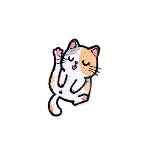 May include: Embroidered patch of a cartoon cat in a playful pose. The cat has a white body with orange and grey fur patches. Its pink paw is raised, and its tongue is sticking out. The patch has a black outline.