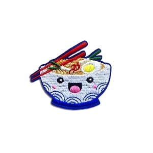 May include: A white bowl with blue and white waves around the rim, filled with noodles, an egg, and red chopsticks. The bowl has a smiling face with pink cheeks.