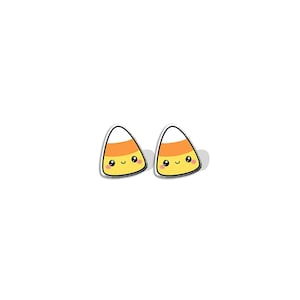 Puede incluir: Dos pendientes con forma de caramelo de maíz con caras sonrientes. Cada pendiente presenta un diseño blanco, naranja y amarillo con un contorno negro. Los pendientes están sobre un fondo blanco, perfectos para Halloween.