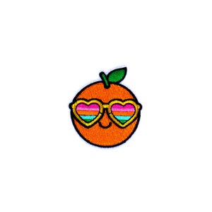 May include: Embroidered patch featuring a smiling orange fruit wearing heart-shaped sunglasses. The orange is a vibrant orange color with a green leaf. The sunglasses have a gold frame and rainbow-colored lenses. The patch is designed for apparel or accessories.
