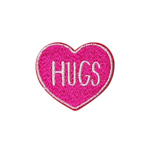 Op de afbeelding: Roze hartvormige patch met witte borduurwerk die "HUGS" zegt.