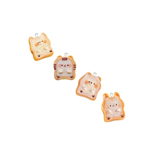 May include: Four charm pendants shaped like slices of bread with cute cartoon cats on them. The charms are made of polymer clay and have a light brown color with white details. Each charm has a silver loop for attaching to a necklace or bracelet.