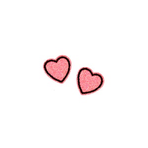 May include: Two pink glitter heart-shaped patches with black outlines. The hearts are set against a white background. These patches could be used for clothing or craft projects.