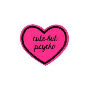 May include: Pink heart-shaped patch with black stitching and the text "cute but psycho" embroidered in black.