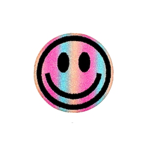 Puede incluir: Un parche redondo de cara sonriente de color arcoíris con contorno negro y purpurina.