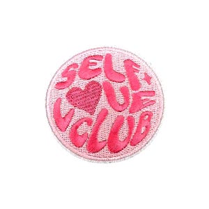 May include: Pink embroidered patch with the text "Self Love Club" in a circular shape with a pink heart in the center.