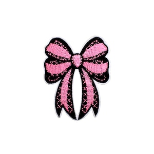 May include: A pink bow patch with black trim and detailing. The bow is embroidered with a textured design, and the edges are outlined in black. The patch is likely for clothing or accessories.