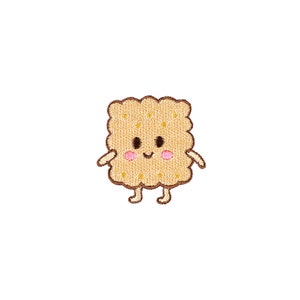 Pode incluir: Um remendo bordado em estilo de desenho animado de um cracker sorridente com olhos castanhos e bochechas rosadas. O cracker é de cor castanho claro com uma superfície texturizada.