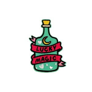 May include: A green glass bottle with a cork stopper and a crescent moon design. The bottle is surrounded by a pink ribbon with the words "LUCKY MAGIC" written on it.