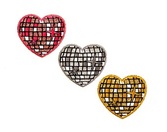 Puede incluir: Tres parches en forma de corazón con un diseño de bola de discoteca. Uno es rojo y marrón, otro es plateado y gris, y el tercero es dorado y blanco. Cada parche tiene un acento en forma de estrella.