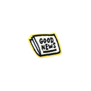 Pode incluir: Um remendo de ferro bordado amarelo com fundo branco e texto preto que diz "GOOD NEWS". O remendo tem a forma de um jornal dobrado.